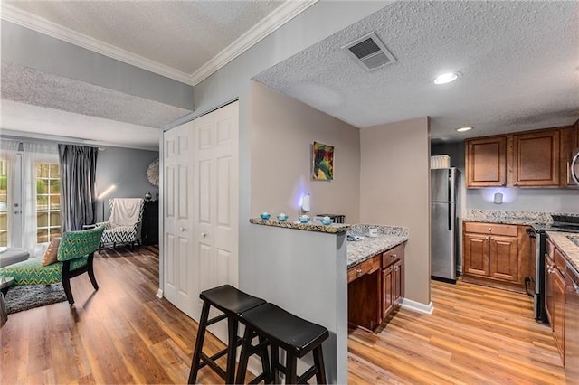 kitchen with a textured ceiling, visible vents, stainless steel appliances, light wood finished floors, and ornamental molding