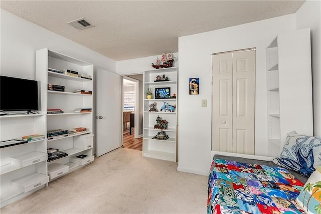 bedroom with a textured ceiling, visible vents, a closet, and light carpet