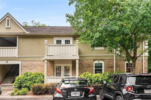 view of front of house featuring brick siding, a balcony, and stucco siding