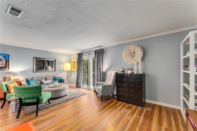living room with a textured ceiling, visible vents, wood finished floors, and crown molding