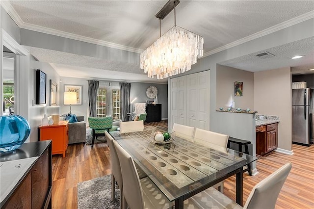 dining space with a textured ceiling, baseboards, an inviting chandelier, light wood-type flooring, and ornamental molding