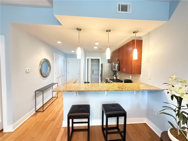 3655 Peachtree Rd NE Unit 304, Atlanta, GA 30319 - kitchen featuring appliances with stainless steel finishes, a peninsula, a breakfast bar, light wood-style flooring, and brown cabinetry