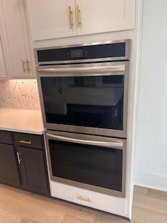 room details with stainless steel double oven, white cabinets, light countertops, and light wood-style flooring