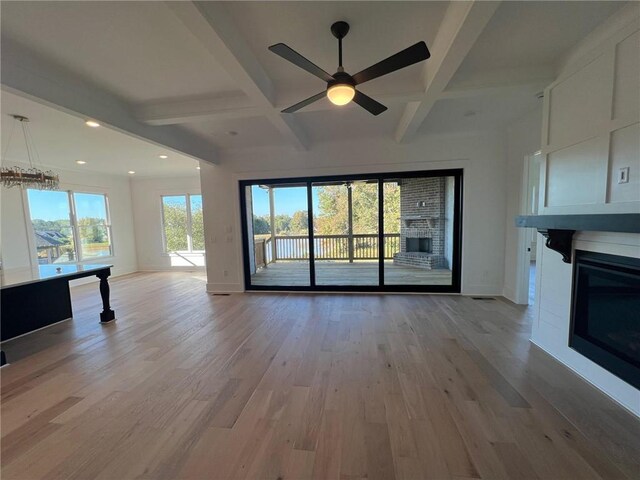 unfurnished living room featuring light wood-style floors, beamed ceiling, and a glass covered fireplace