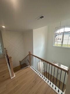 corridor featuring visible vents, an upstairs landing, and wood finished floors