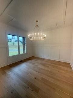 unfurnished dining area with a wainscoted wall, a chandelier, a decorative wall, and wood finished floors