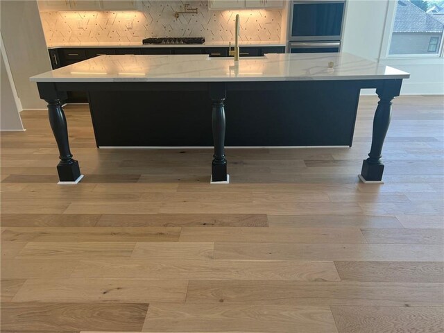 interior details with a breakfast bar area, light wood-style floors, double oven, a sink, and an island with sink