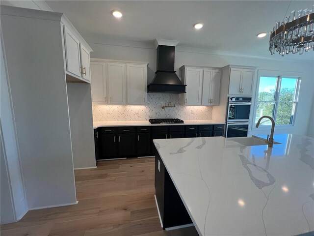 kitchen featuring stainless steel appliances, custom range hood, white cabinetry, a sink, and dark cabinets