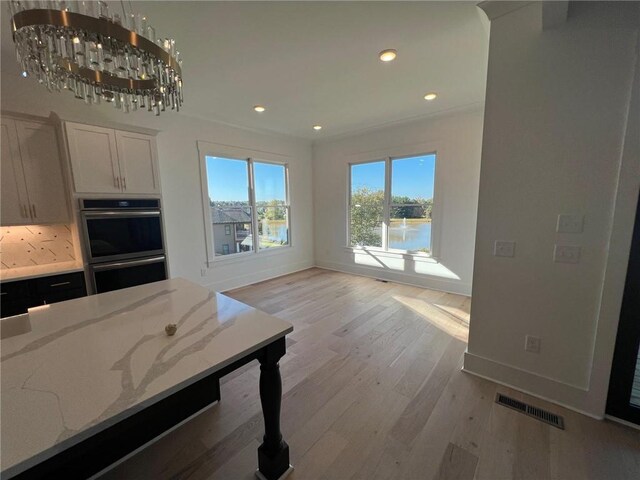 kitchen featuring visible vents, light wood-style flooring, light stone counters, stainless steel double oven, and white cabinetry