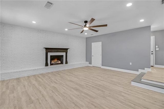 unfurnished living room with a ceiling fan, a fireplace, visible vents, and light wood-style floors