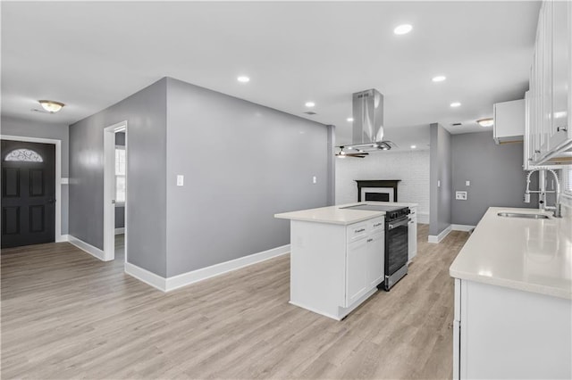 kitchen with a fireplace, a sink, white cabinetry, stainless steel electric stove, and island exhaust hood