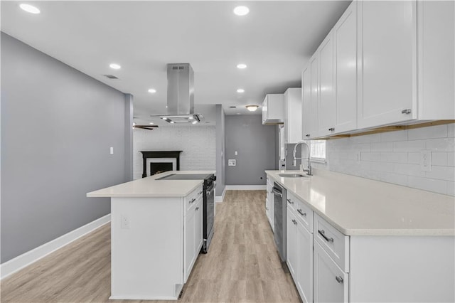 kitchen with a fireplace, white cabinets, appliances with stainless steel finishes, tasteful backsplash, and island exhaust hood