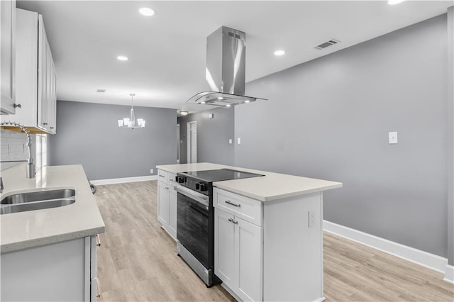 kitchen with a sink, visible vents, white cabinetry, stainless steel electric range oven, and island exhaust hood