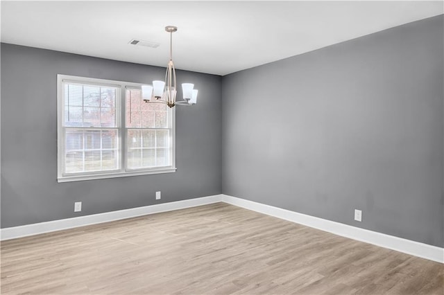 spare room with light wood-style floors, visible vents, baseboards, and an inviting chandelier