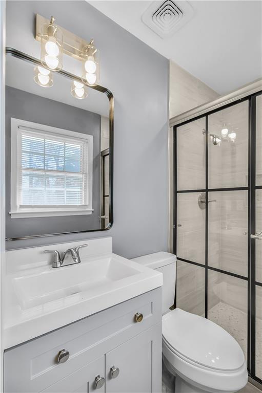 bathroom featuring toilet, a shower stall, visible vents, and vanity