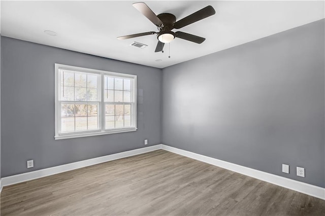 unfurnished room with a ceiling fan, visible vents, baseboards, and wood finished floors