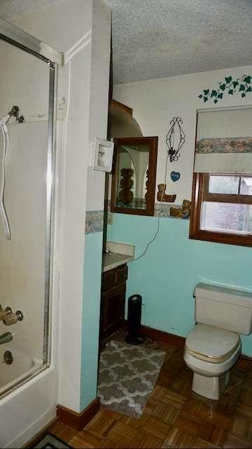 full bathroom featuring vanity, shower / bath combination with glass door, a textured ceiling, and parquet floors