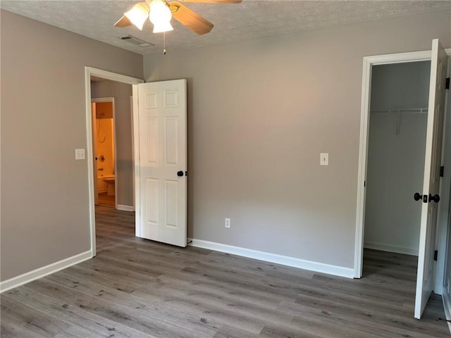 7454 Woody Springs Dr, Flowery Branch, GA 30542 - unfurnished bedroom featuring wood finished floors, a textured ceiling, a spacious closet, a closet, and baseboards