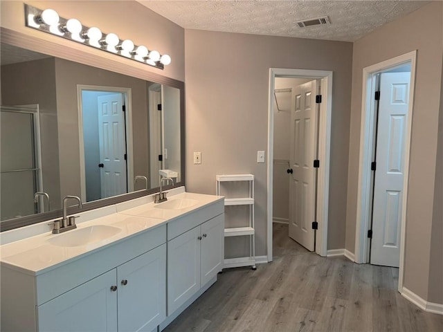 7454 Woody Springs Dr, Flowery Branch, GA 30542 - full bathroom featuring wood finished floors, double vanity, an enclosed shower, a textured ceiling, and baseboards