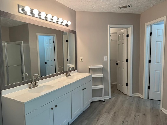7454 Woody Springs Dr, Flowery Branch, GA 30542 - bathroom featuring wood finished floors, a stall shower, double vanity, a textured ceiling, and baseboards
