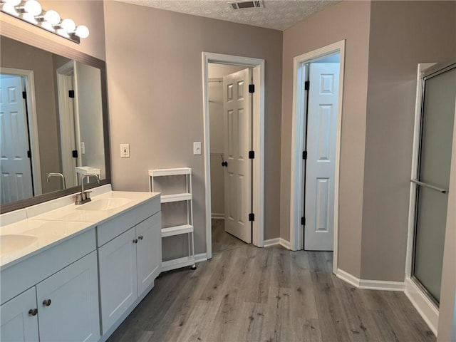 7454 Woody Springs Dr, Flowery Branch, GA 30542 - bathroom with wood finished floors, a shower stall, double vanity, baseboards, and a textured ceiling
