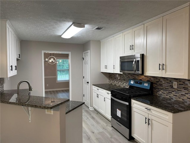 7454 Woody Springs Dr, Flowery Branch, GA 30542 - kitchen featuring stainless steel appliances, light wood finished floors, a peninsula, decorative backsplash, and dark stone counters