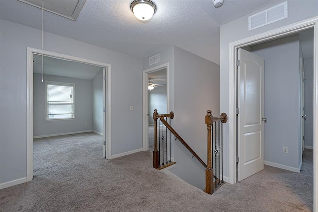 corridor with visible vents, an upstairs landing, attic access, and carpet flooring