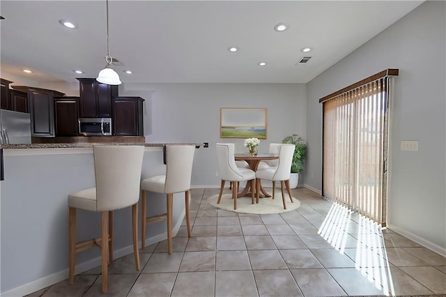 kitchen with dark brown cabinets, a kitchen bar, light tile patterned floors, recessed lighting, and appliances with stainless steel finishes