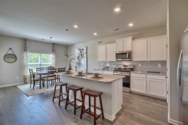 kitchen featuring white cabinets, appliances with stainless steel finishes, wood finished floors, a kitchen island with sink, and backsplash