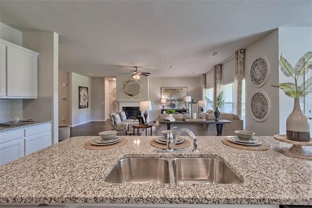 kitchen featuring light stone counters, a fireplace, open floor plan, white cabinetry, and a sink