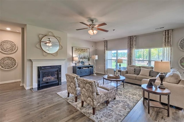 living area with wood finished floors, a ceiling fan, visible vents, baseboards, and a glass covered fireplace