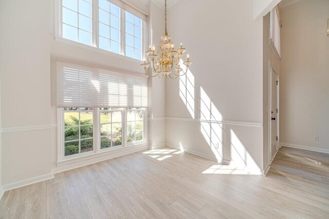 unfurnished living room with a notable chandelier, light hardwood / wood-style floors, and a high ceiling