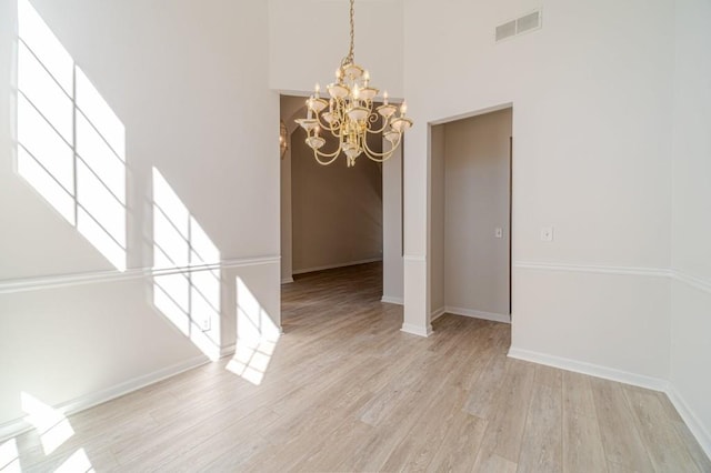 unfurnished dining area featuring an inviting chandelier, a high ceiling, and light wood-type flooring