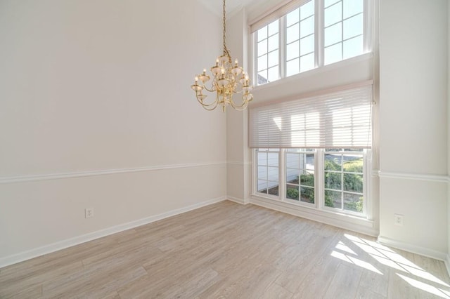 spare room featuring a high ceiling, light hardwood / wood-style flooring, and a notable chandelier