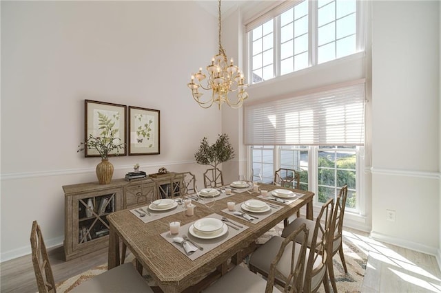 dining area with a towering ceiling, light hardwood / wood-style floors, and a notable chandelier