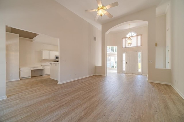 unfurnished living room with a towering ceiling, ceiling fan with notable chandelier, and light hardwood / wood-style flooring