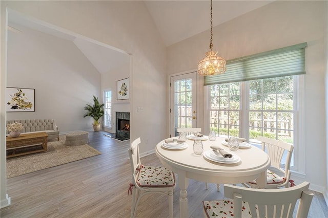 dining room featuring hardwood / wood-style flooring, high vaulted ceiling, a chandelier, and a fireplace