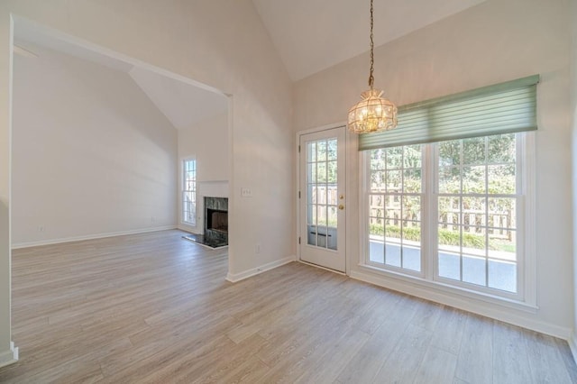 unfurnished living room featuring high vaulted ceiling, an inviting chandelier, a high end fireplace, and light hardwood / wood-style flooring