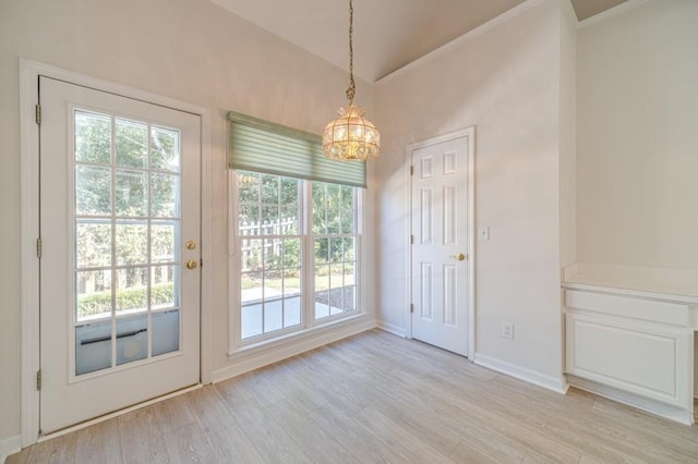 doorway with an inviting chandelier, light hardwood / wood-style flooring, and vaulted ceiling