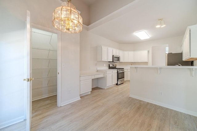 kitchen featuring appliances with stainless steel finishes, pendant lighting, white cabinets, a kitchen breakfast bar, and light hardwood / wood-style floors