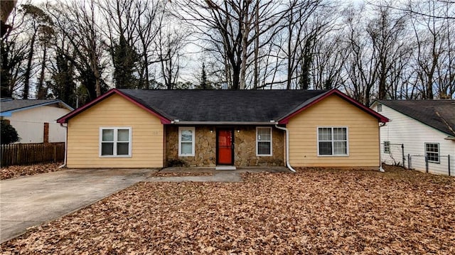 ranch-style house with stone siding, concrete driveway, and fence