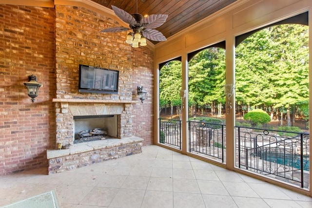 unfurnished sunroom featuring ceiling fan, wood ceiling, and an outdoor stone fireplace