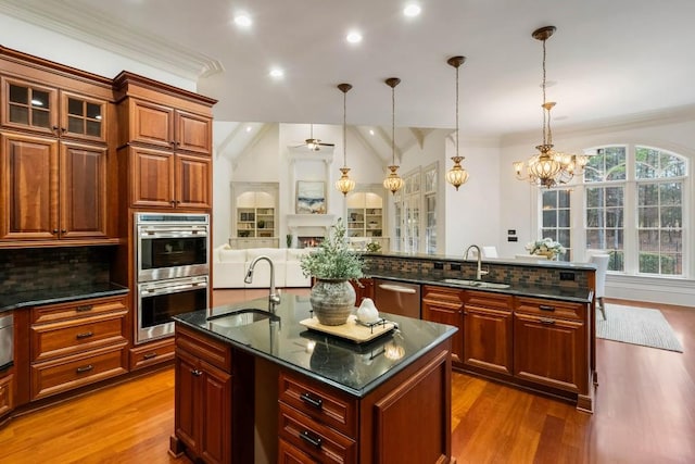 kitchen with sink, vaulted ceiling, decorative light fixtures, a kitchen island with sink, and appliances with stainless steel finishes