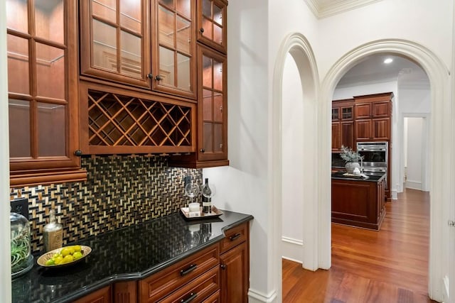 bar with decorative backsplash, hardwood / wood-style flooring, oven, and dark stone countertops