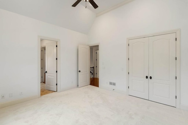 unfurnished bedroom featuring ceiling fan, a closet, high vaulted ceiling, and light colored carpet