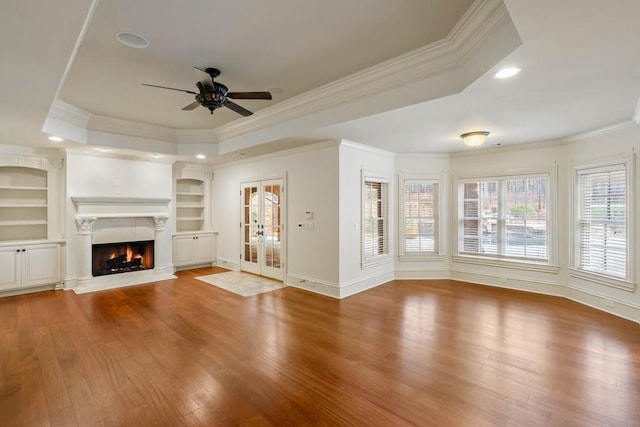 unfurnished living room featuring hardwood / wood-style floors, a tray ceiling, built in shelves, and ornamental molding