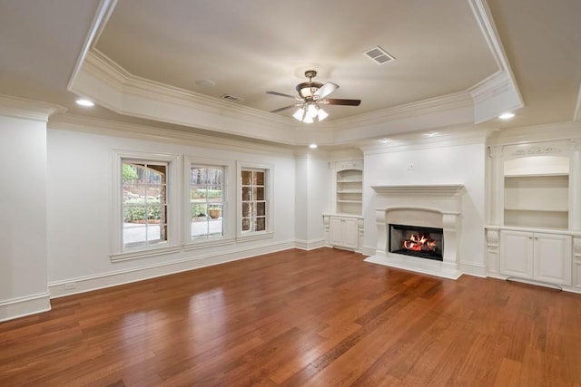 unfurnished living room featuring ornamental molding, a raised ceiling, ceiling fan, hardwood / wood-style flooring, and built in features