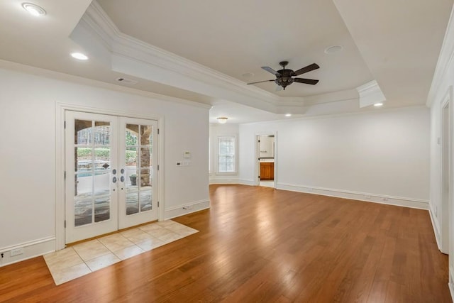 unfurnished room featuring a raised ceiling, light wood-type flooring, ornamental molding, and french doors