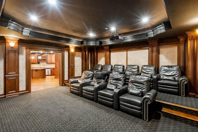 carpeted home theater with a raised ceiling, ornamental molding, and decorative columns