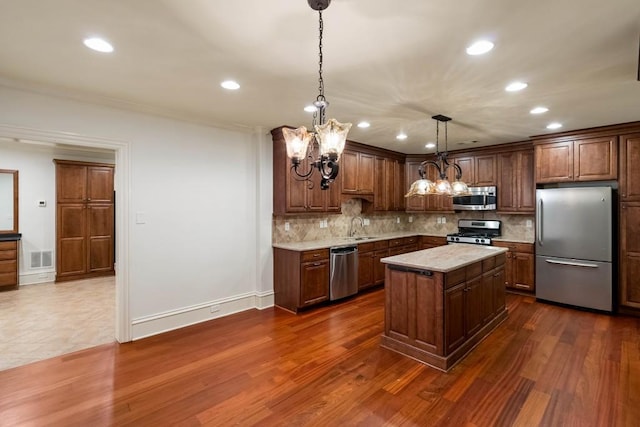 kitchen featuring appliances with stainless steel finishes, sink, decorative light fixtures, dark hardwood / wood-style floors, and a kitchen island